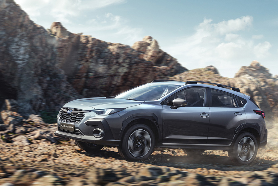 Subaru Crosstrek važiuoja žvyrkeliu, už automobilio kyla dulkių debesys.