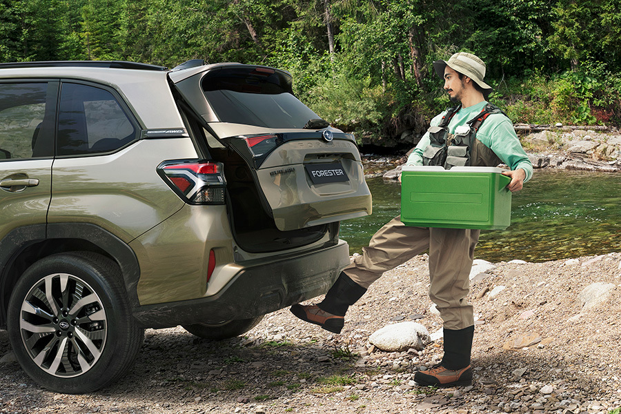 Subaru su bekontakte bagažinės atidarymo funkcija – vyras su žvejybos apranga aktyvuoja jutiklį koja, kad galėtų atidaryti bagažinę nenaudodamas rankų.