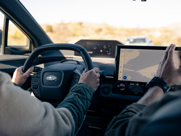Subaru salonas su vairuotoju prie vairo ir navigacijos žemėlapiu automobilio jutikliniame ekrane.